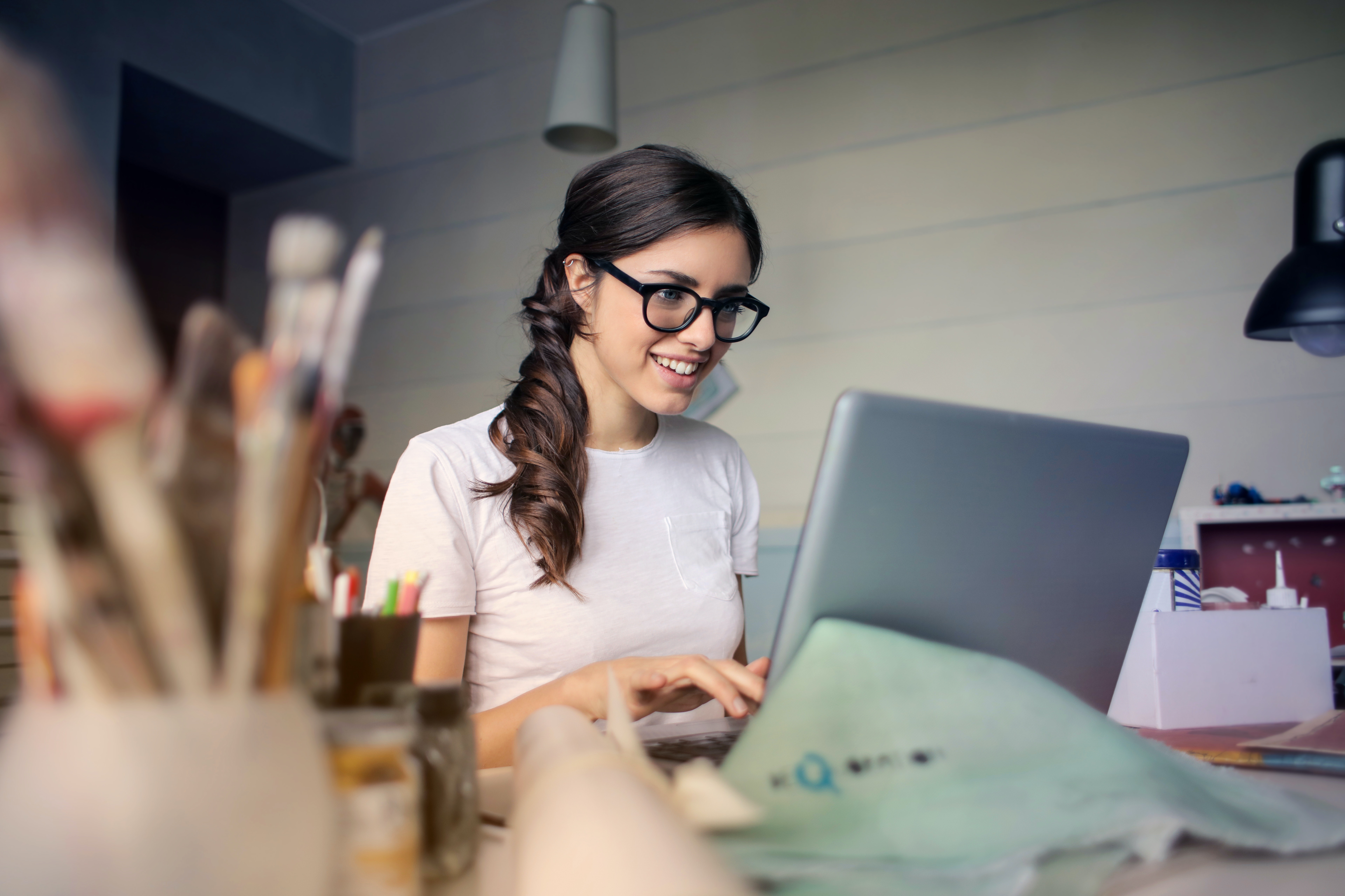 Νεαρή γυναίκα εργάζεται χαμογελαστή στο laptop σε γραφείο.